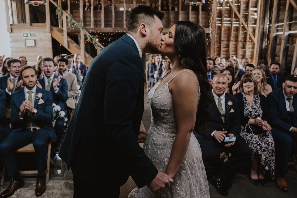 First kiss in the ceremony barn at The Barns at Lodge Farm in Essex.