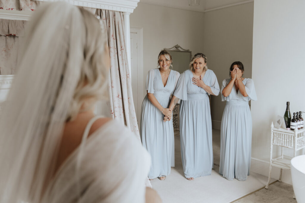 The bridesmaids reacting to the bride in her dress at the bridal suite at Butley Priory