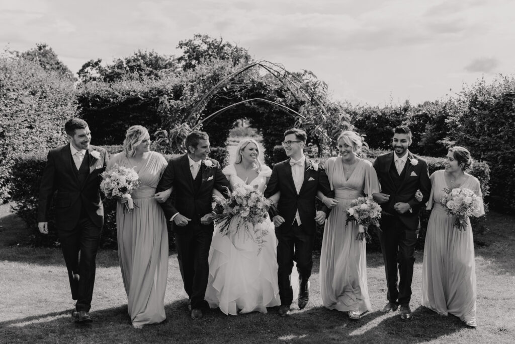 The bridesmaids and groomsmen walking towards the camera in the gardens at Butley Priory