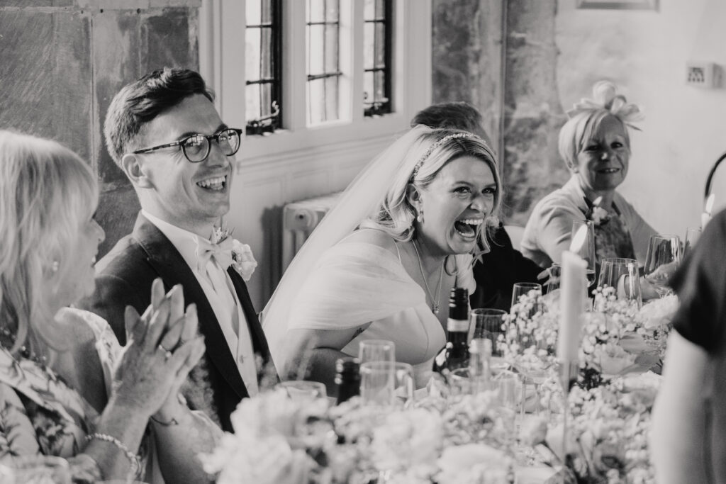 The newlywed couple laughing during speeches at Butley Priory