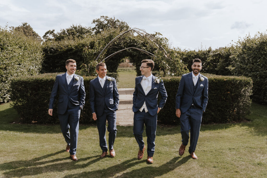 The groom and his groomsmen walking towards the camera during formal photos at Butley Priory