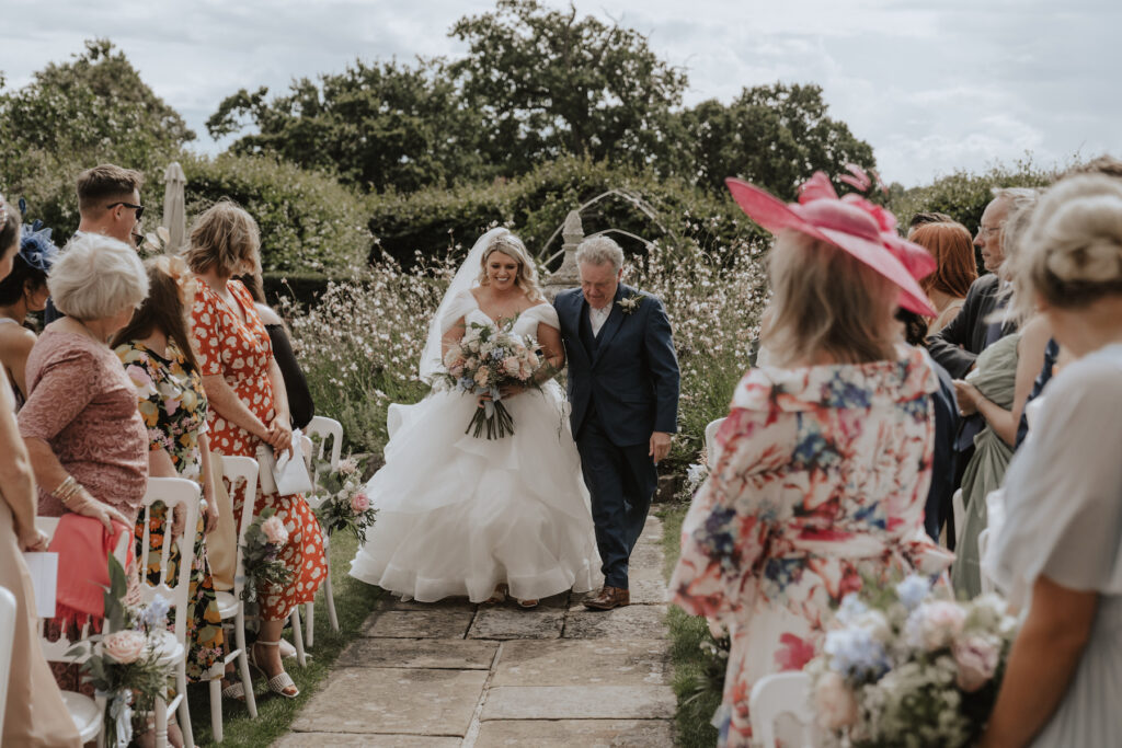 The bride walking down the aisle for her outdoor ceremony at Butley Priory