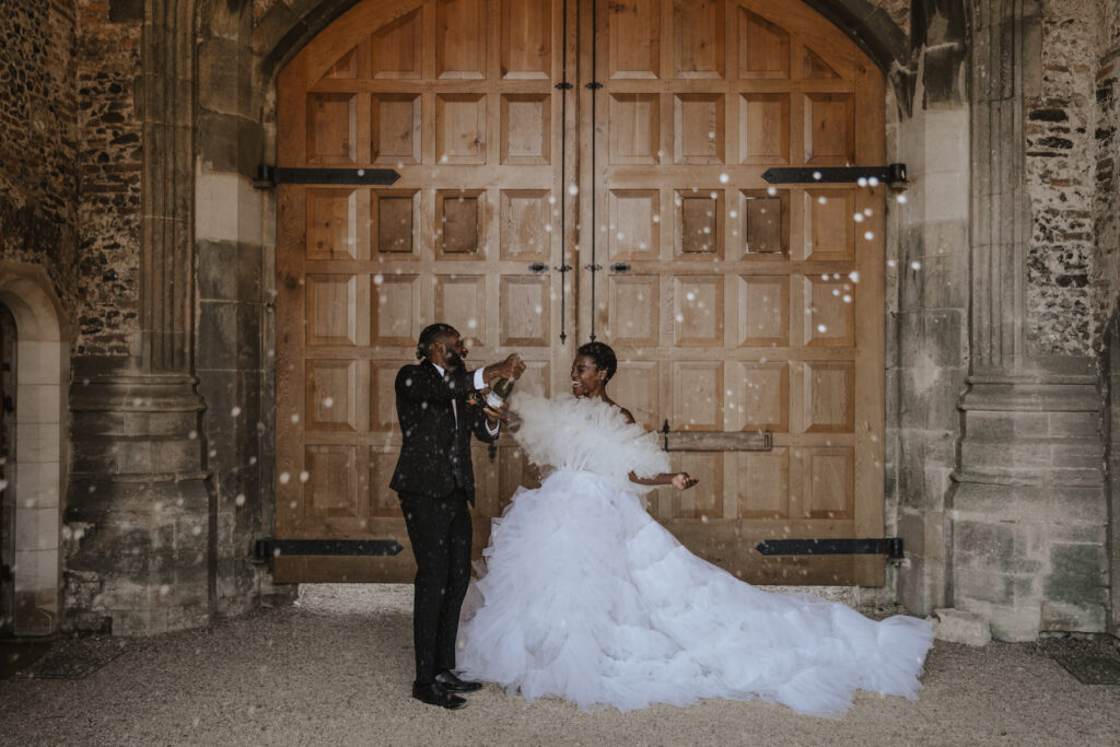 The couple spraying champagne during their couples portraits at Pentney Abbey