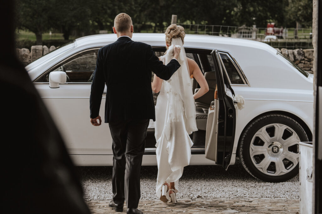 The groom helping his bride into the car at The Tithe Barn in Yorkshire