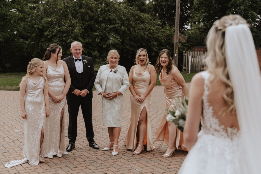 The bride doing a first look with her bridesmaids and parents outside at Swallows Nest Barn in Northamptonshire