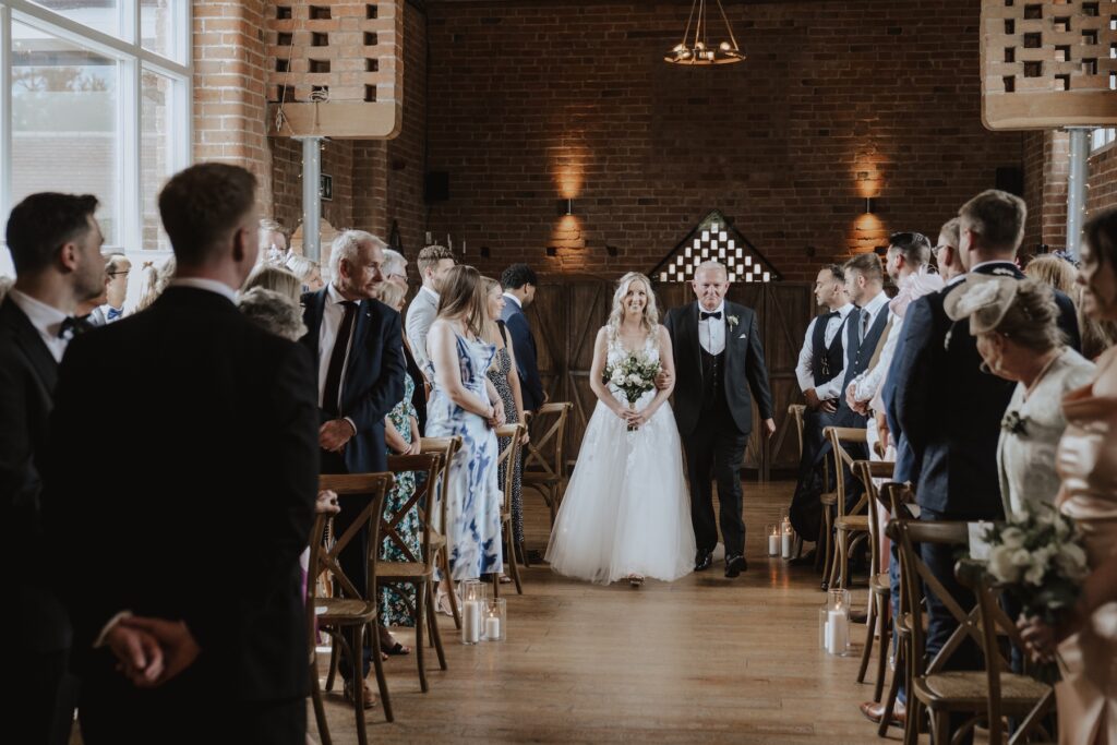 The bride walking down the aisle at Swallows Nest Barn in Northamptonshire