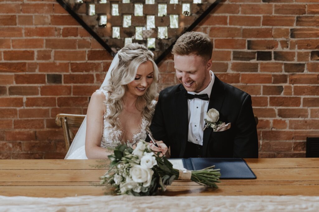 The couple singing the wedding register after the ceremony at Swallows Nest Barn in Northamptonshire