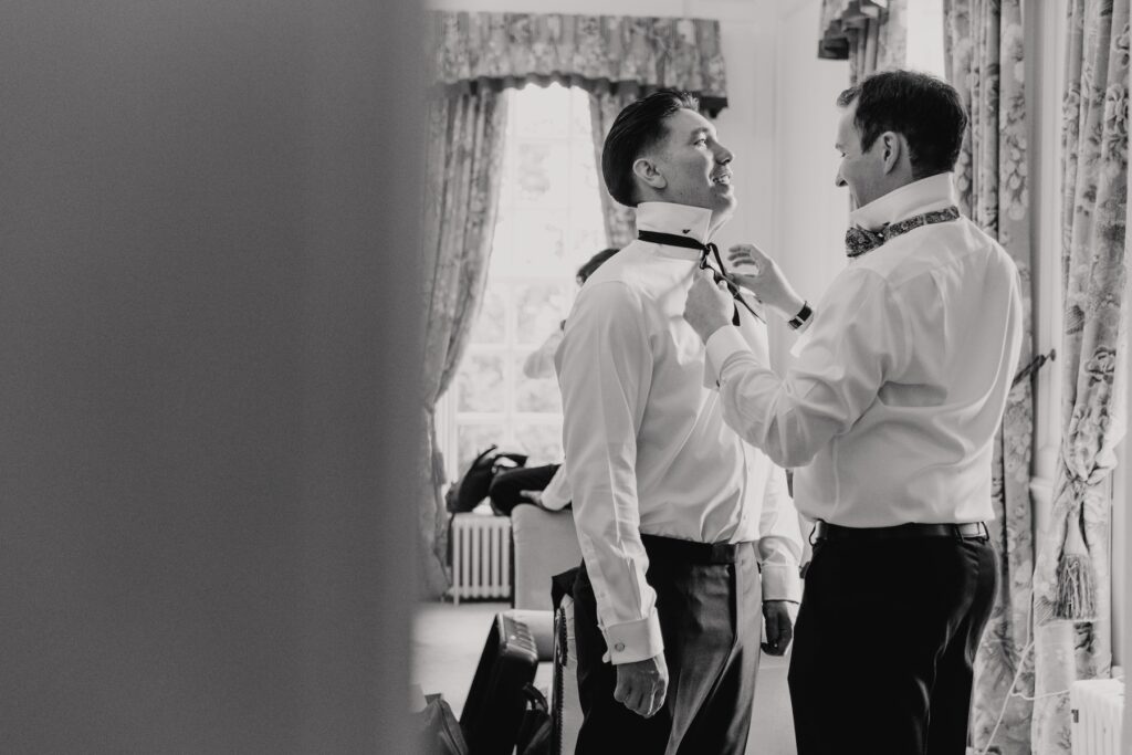 The groom putting on his tie at the groom's suite at Gosfield Hall