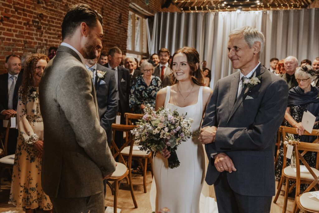 Bride walking down the aisle in the warm, rustic hall at Copdock Hall wedding