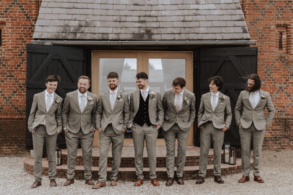Groomsmen posing and joking during formal photos at Copdock Hall terrace