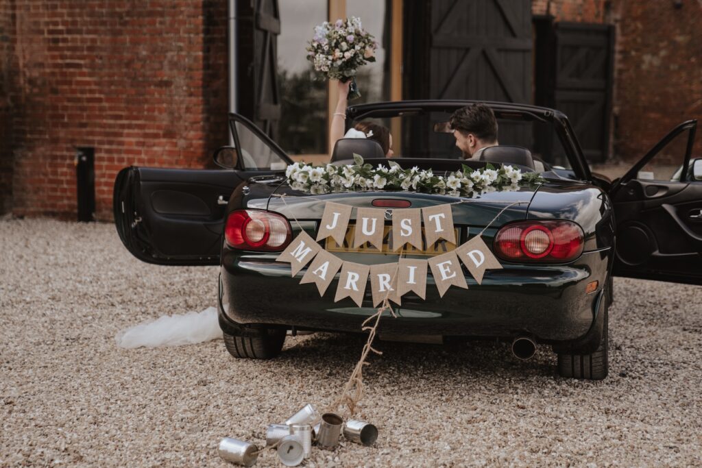 Bride and groom smiling next to sports car surprise outside Copdock Hall