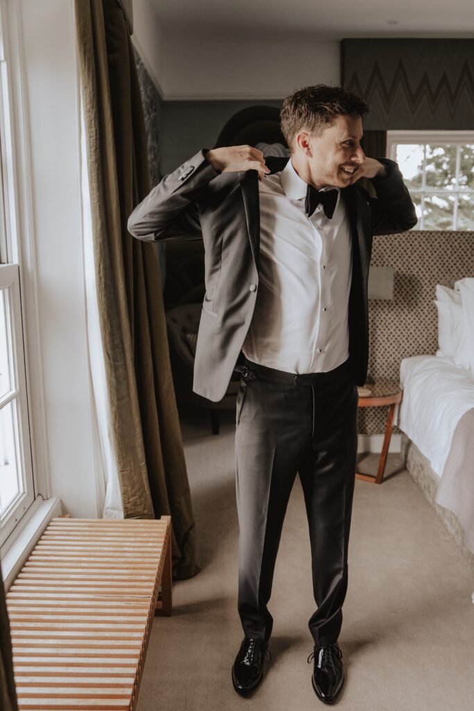 Groom adjusting bow tie in Godwick Hall house before wedding ceremony