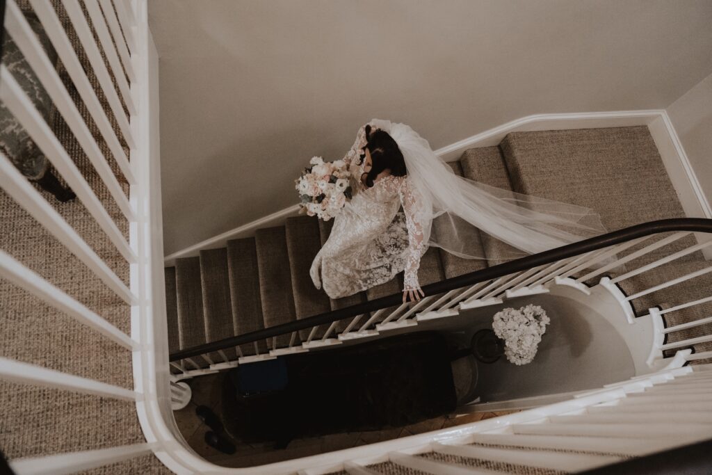 The bride going down the stairs in the house at Godwick Hall in her wedding dress