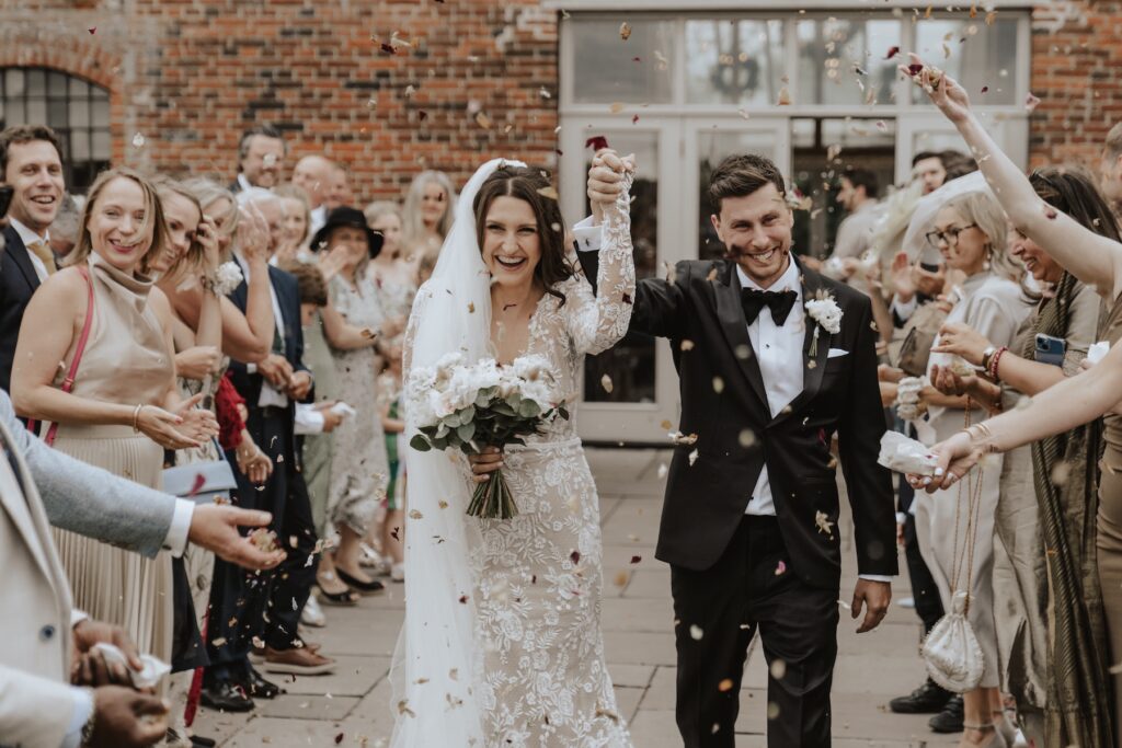 Confetti flying outside Godwick Hall brick barn after ceremony