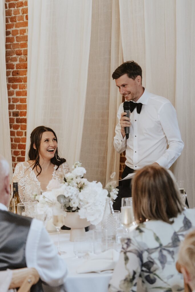 Bride and groom listening to heartfelt wedding speeches in the barn