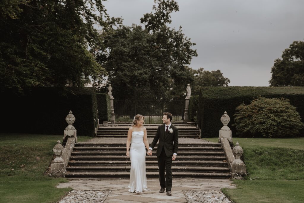 Bride and groom walking hand-in-hand through the gardens at Hengrave Hall.