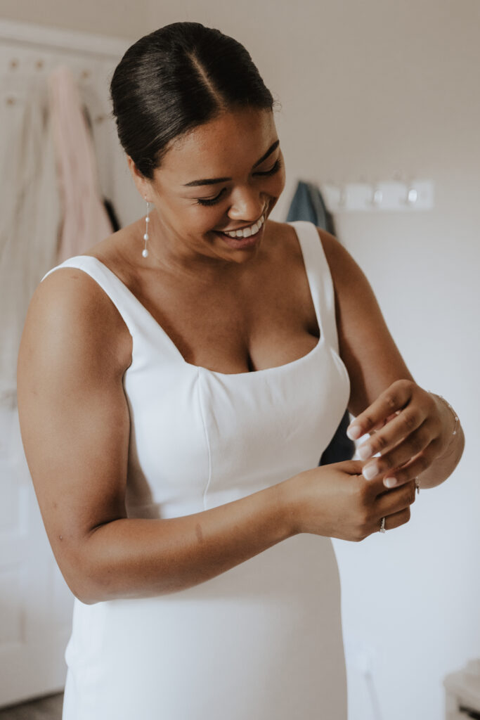Bride smiling as she puts her bracelet on at her parents’ home
