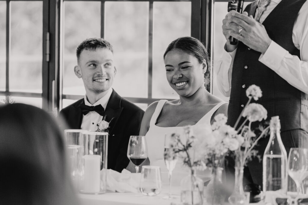 Bride and groom holding hands under the table while smiling during speeches