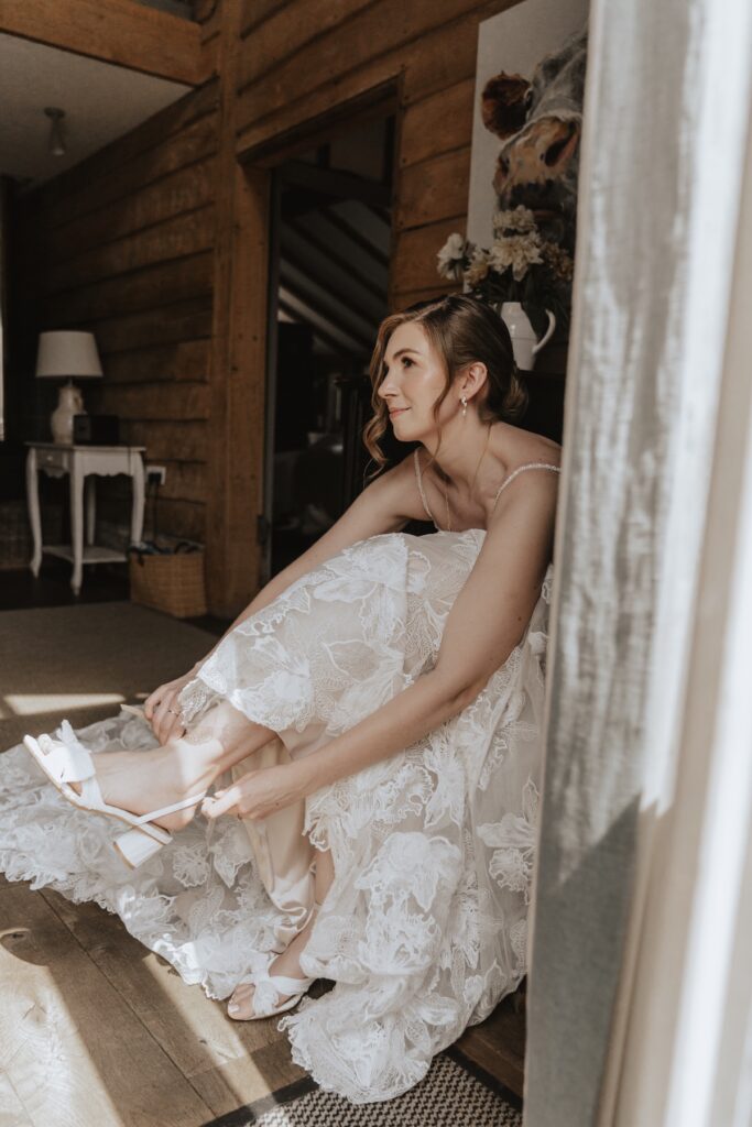 Bride putting on her wedding dress hanging by rustic beams at Retreat East, Suffolk countryside