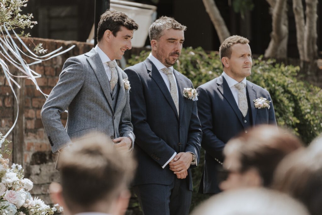 The groom standing at the outdoor ceremony setup at Jimmy’s Farm with parasols and summer florals