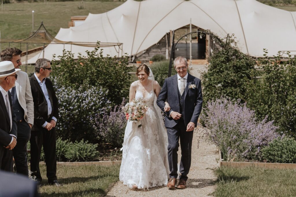 Bride walking down the aisle from Jimmy’s Farm stretch tent in the sunshine