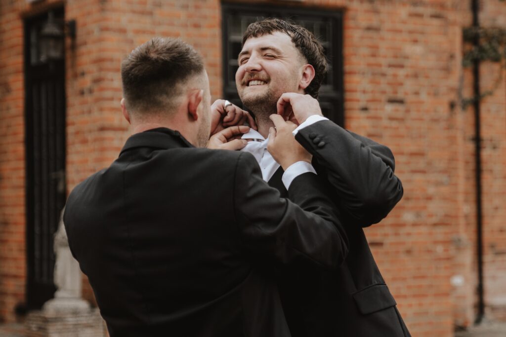 Groom adjusting his bow tie outside in Seckford Hall gardens