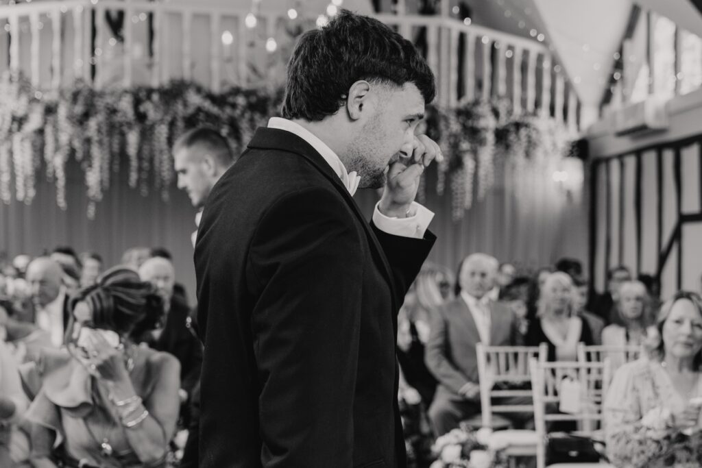 Groom wiping a tear as he sees his bride enter the ceremony room