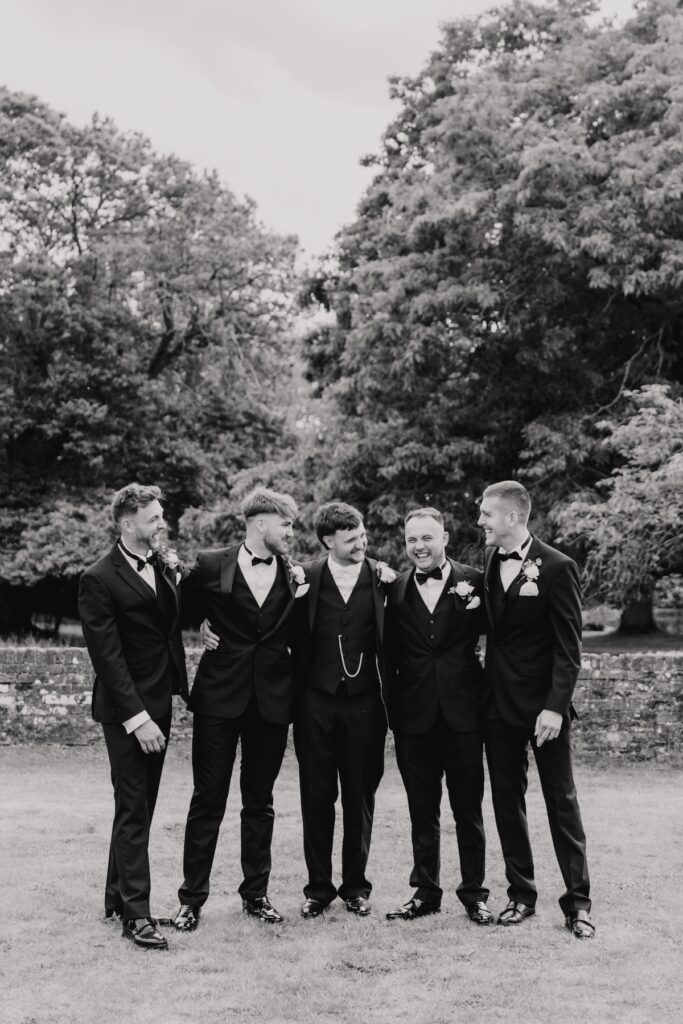 Groomsmen sharing a laugh while pinning on buttonholes outdoors