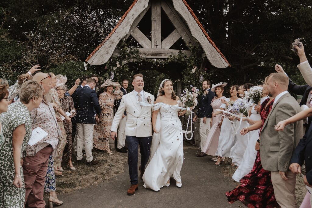 Joyful confetti moment outside the church with petals caught in the wind