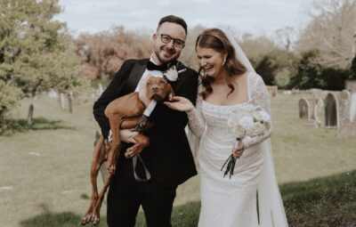 A bride and groom laughing and holding their dog on their wedding day in Kent