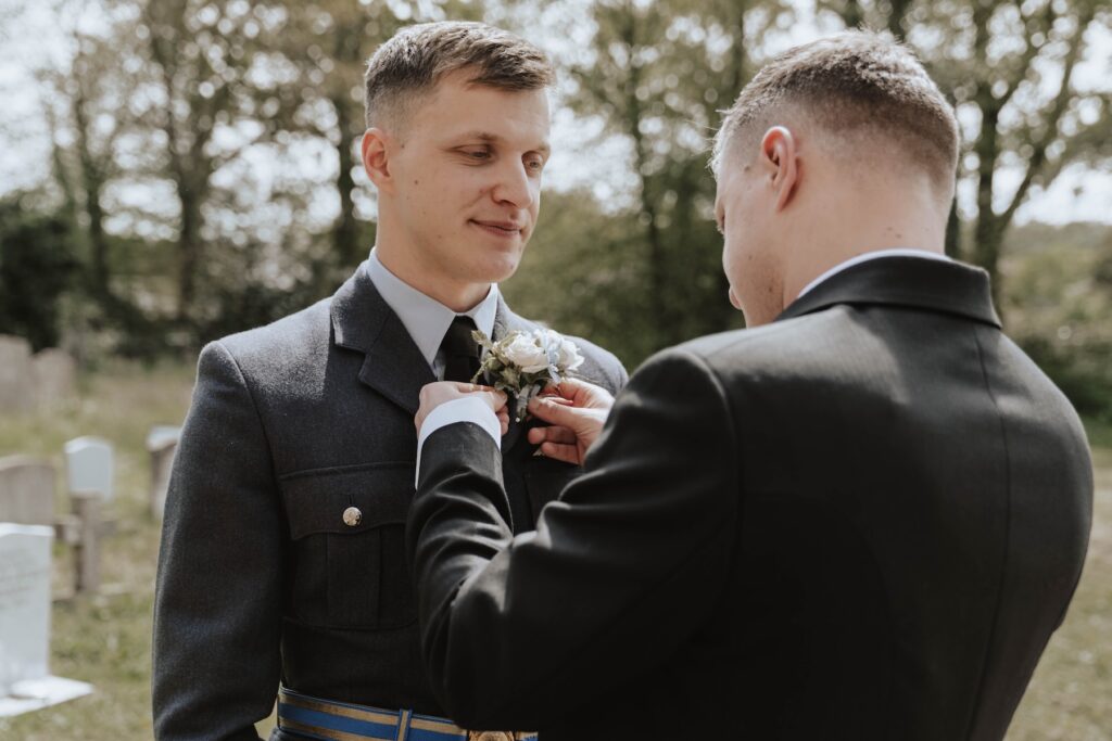 A groom getting his buttonhole put on in Woodbridge outside a church