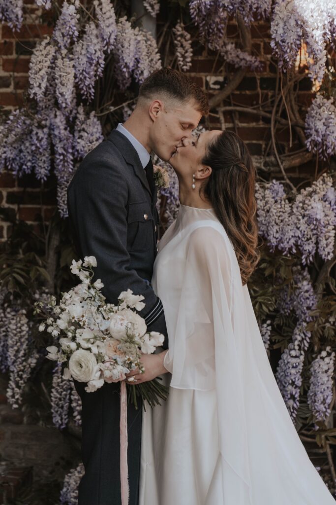 Couples portraits taken of a bride and groom on their wedding day outside Seckford Hall with the wisteria