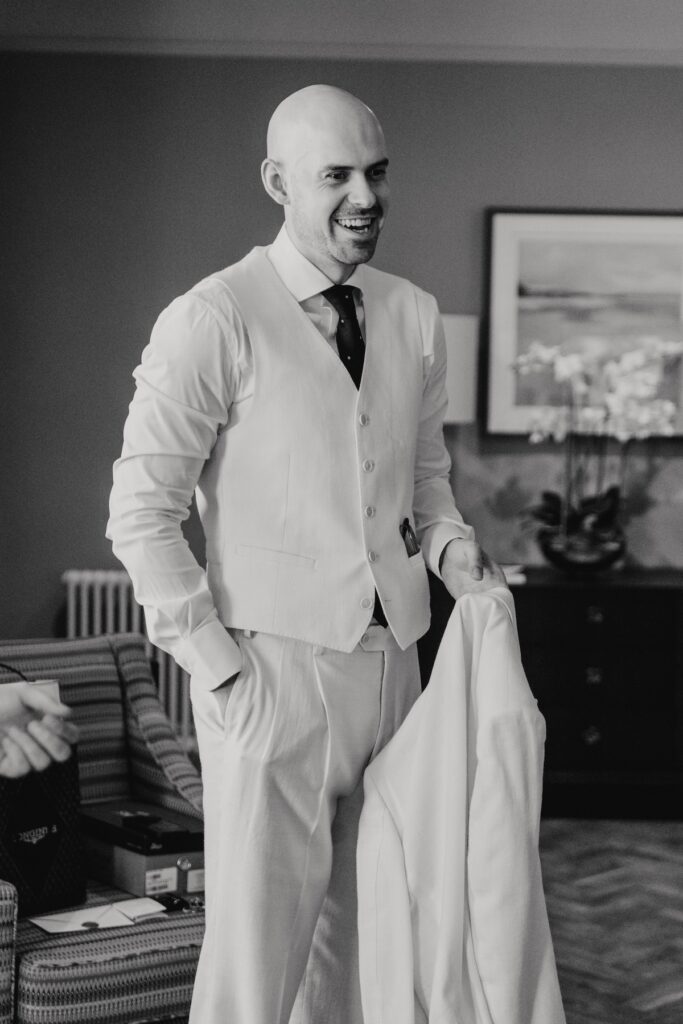 Groom wearing a cream wedding suit at Cornwallis House before his Marquis Suffolk wedding