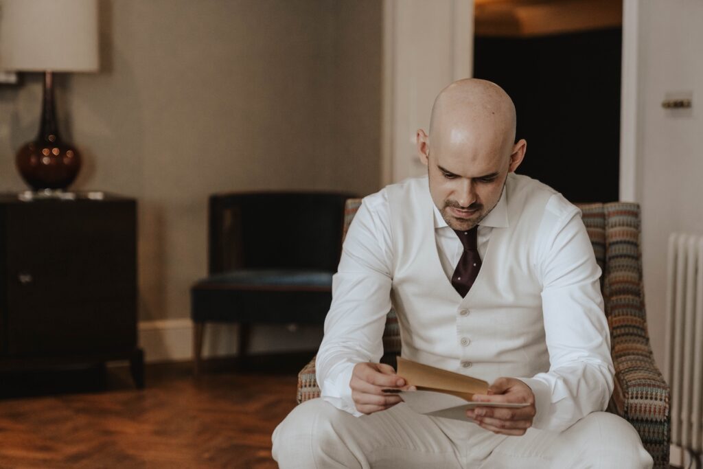 Groom buttoning up his cream wedding suit before his wedding at Marquis Suffolk