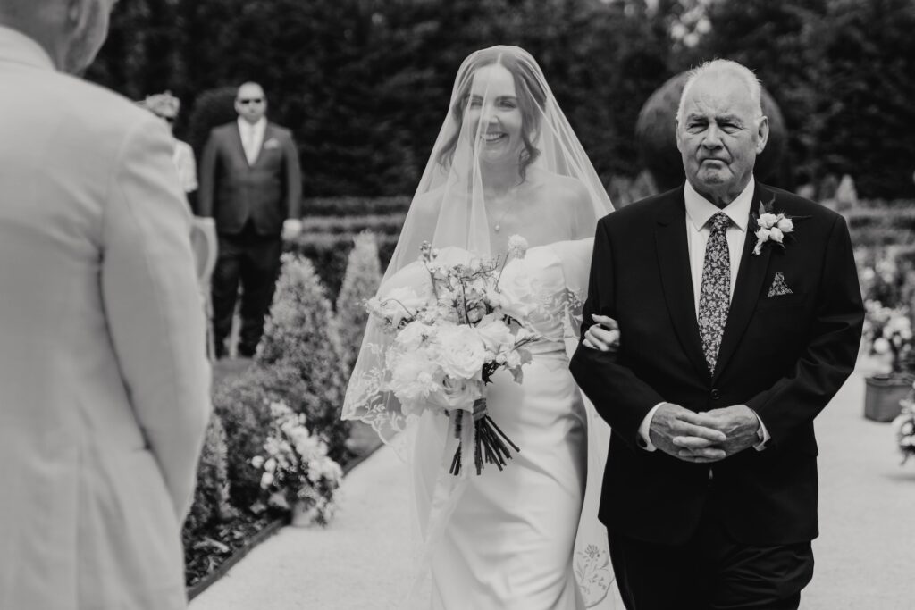 Bride walking towards her groom during an outdoor ceremony at Marquis Suffolk