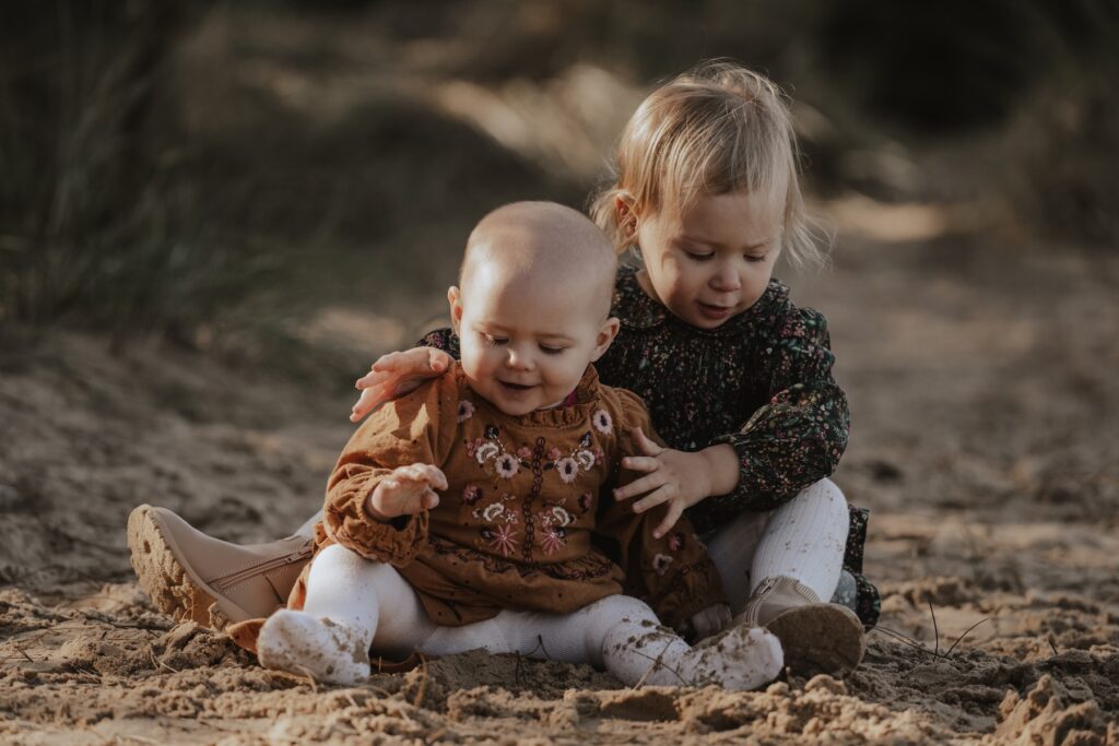Two sisters laughing and playing together in the woodland at Holkham Beach