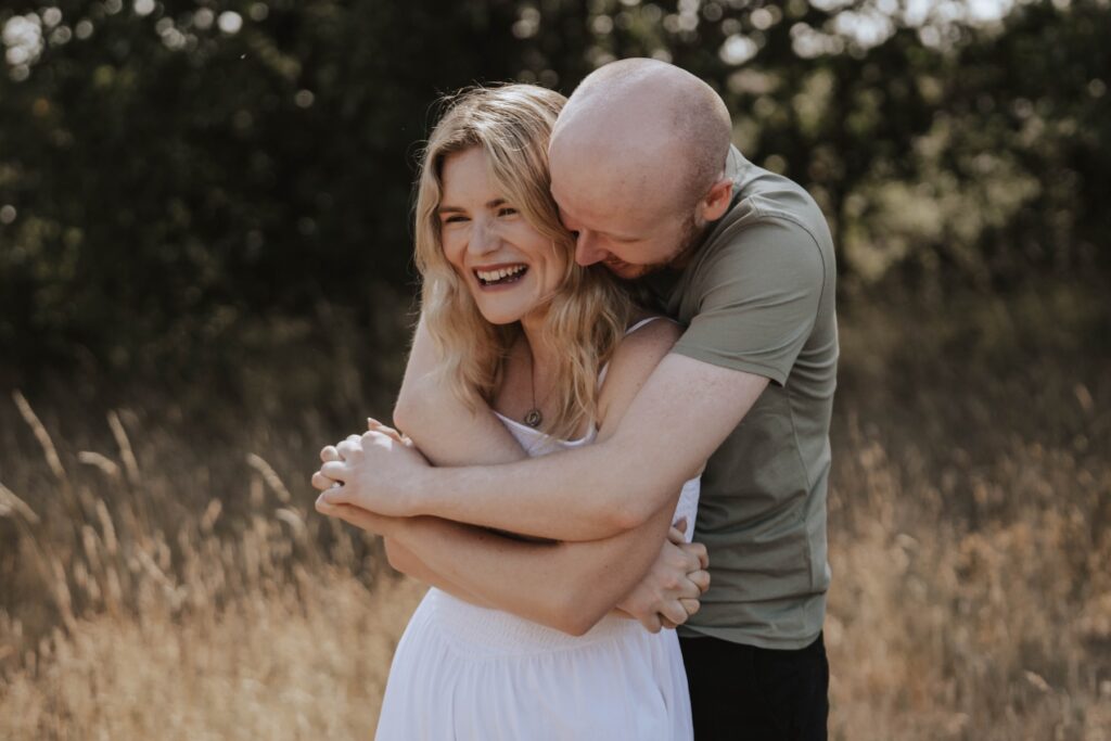 Couple embracing beside the water during their Snape Maltings engagement session in Suffolk