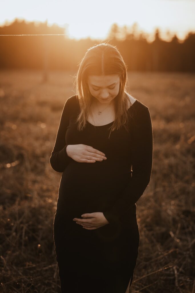 Couple expecting their first baby standing together in the woodland at golden hour